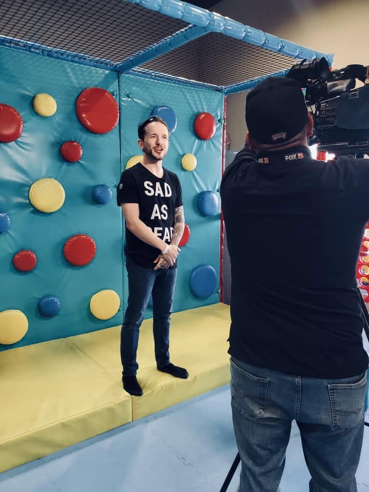 Cash being filmed by a FOX5 Las Vegas camera operator inside a colorful inflatable sensory play structure, mid-interview.